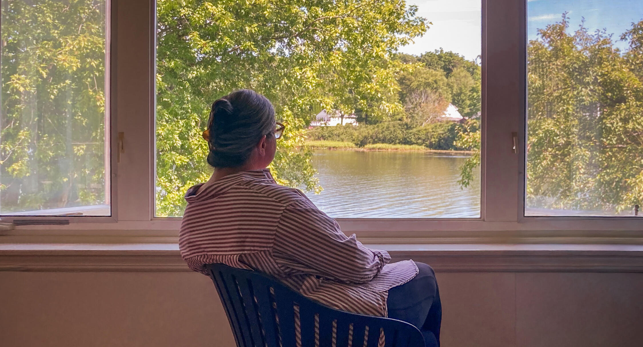 Woman sitting in a chair, looking out the window over a lake.